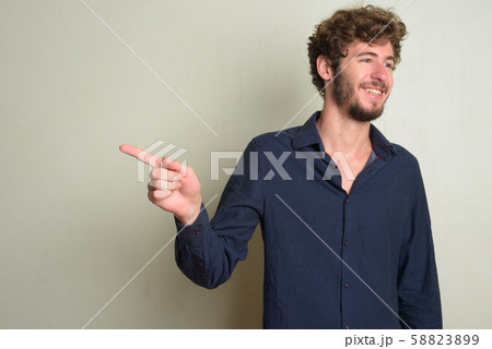 Happy young bearded businessman with curly hair pointing finger and looking away 58823899