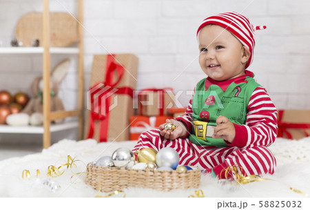 Sweet baby in elf costume playing with Christmas decorations 58825032