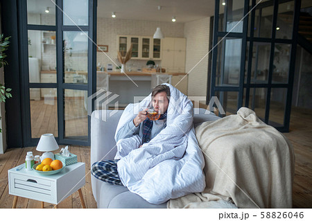 Man feeling cold so drinking hot tea and covering in bedsheet Man feeling cold so drinking hot tea and covering in bedsheet 58826046