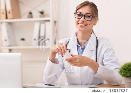 Smiling Doctor Woman Holding Prescribed Medication Jar Sitting In Office Smiling Doctor Woman Holding Prescribed Medication Jar Sitting In Office 58837327