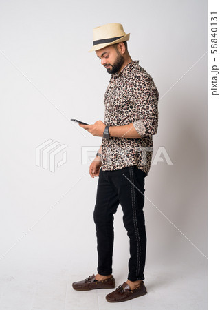 Full body shot profile view of young bearded Indian man using phone 58840131