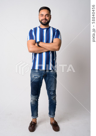 Full body shot of happy young bearded Indian man smiling with arms crossed 58840456