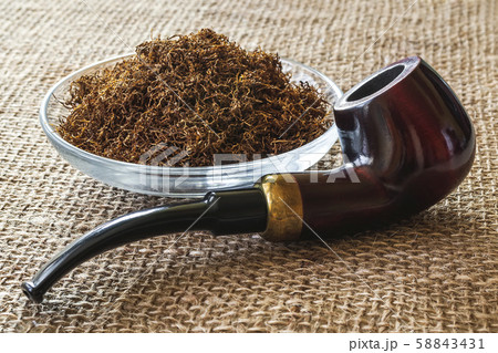 Wooden pipe near heap of tobacco in a glass bowl on a sackcloth background. 58843431