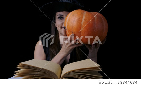 Beautiful sexy woman in a black witch costume and hat holding a pumpkin. Halloween holiday party 58844684