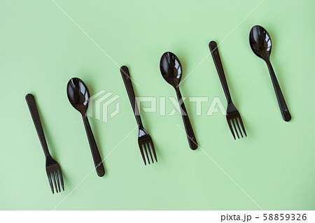 Black plastic spoons and forks lay on a green background in neo light 58859326