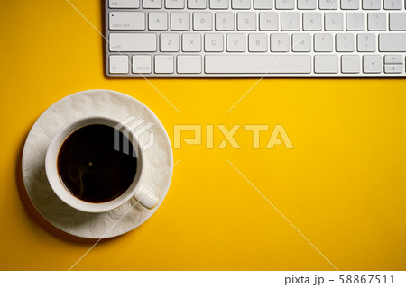 Top view of white keyboard and cup of coffee on yellow desk Top view of white keyboard and cup of coffee on yellow desk 58867511