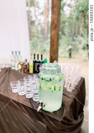 Lemonade jar and glasses for alcohol drinks on wooden table outdoors. Rustic catering at wedding 58868385