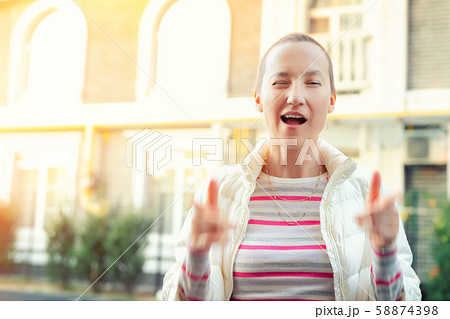 Happy caucasian young adult hipster girl portrait winking and showing thums up sign outdoors at warm 58874398
