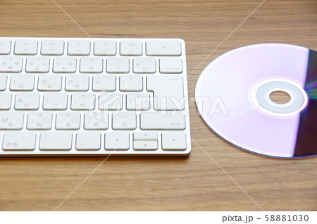 木のデスクに置かれた白いキーボードとCD-ROM 58881030