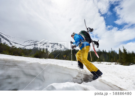 Side view of male in winter mountain touring walking up with ski poles, backpack and snowboard on Side view of male in winter mountain touring walking up with ski poles, backpack and snowboard on 58886480
