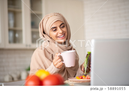 Beautiful Muslim girl having a video call while enjoying her dinner 58891055