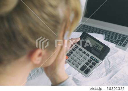 Woman uses a calculator to sum up expenses at home Woman uses a calculator to sum up expenses at home 58891323