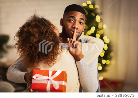 Shh! Afro man giving Christmas present to woman Shh! Afro man giving Christmas present to woman 58895075