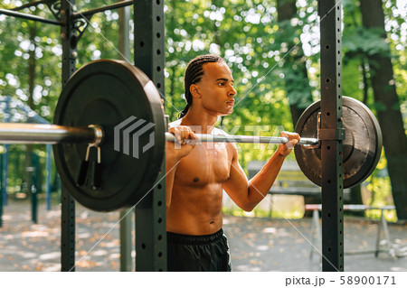 Young man leaning over weight bar after training outdoors 58900171