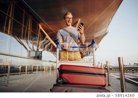 Excited young man with phone luggage near airport stock photo 58914260