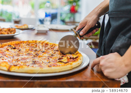 Closeup hand of chef cutting pizza on table. Closeup hand of chef cutting pizza on table. 58914670