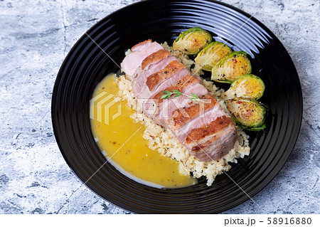 Grilled duck with fried Brussels sprouts, rice from cauliflower and orange sauce on a black plate. Close-up, selective focus. Grilled duck with fried Brussels sprouts, rice from cauliflower and orange sauce on a black plate. Close-up, selective focus. 58916880