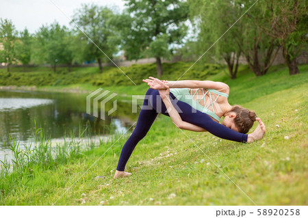 A young sports girl practices yoga on a green lawn 58920258