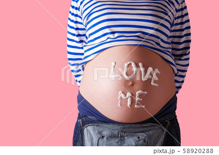Pregnant woman writing 'love me' word on her belly. Trendy Pink background. Pregnant woman writing 'love me' word on her belly. Trendy Pink background. 58920288