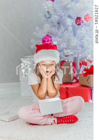 Happy girl opens a magical glowing Christmas gift while sitting near Christmas tree Happy girl opens a magical glowing Christmas gift while sitting near Christmas tree 58921627