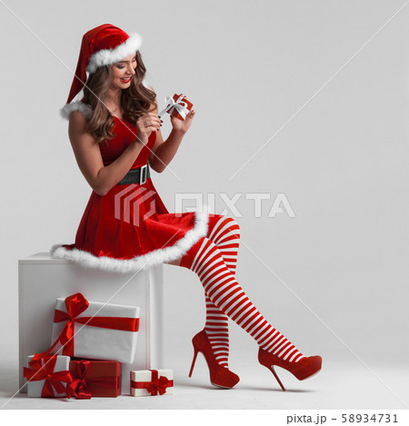 Girl in santa dress unwrapping gift 58934731
