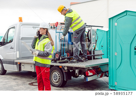 Workers taking care of a delivery of mobile rental toilets 58935177