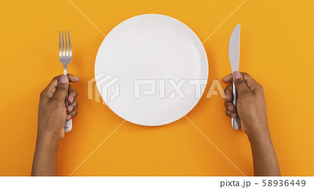Empty plate and cutlery in woman's hands on orange background Empty plate and cutlery in woman's hands on orange background 58936449