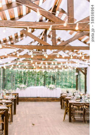 Rustic tent restaurant with wedding or dinner table and floral decorations and light bulbs, on a Rustic tent restaurant with wedding or dinner table and floral decorations and light bulbs, on a 58936964