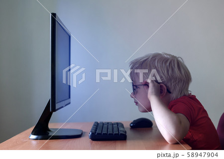 Blond boy with glasses sits his nose buried in a Blond boy with glasses sits his nose buried in a 58947904