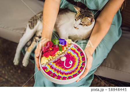 Young woman having a mediterranean breakfast seated at her sofa and with her cat and eats Healthy 58948445