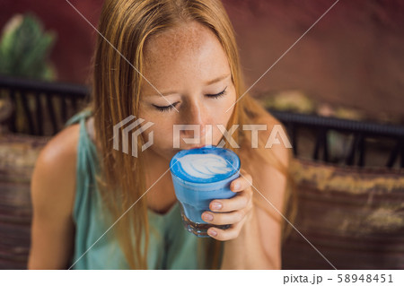 Young woman having a mediterranean breakfast seated at sofa and drinks Trendy drink: Blue latte. Hot Young woman having a mediterranean breakfast seated at sofa and drinks Trendy drink: Blue latte. Hot 58948451