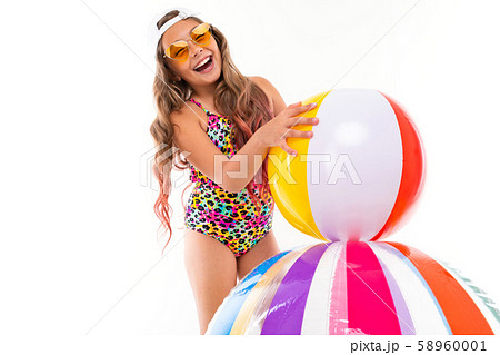 Happy young girl in bathing suit, sunglasses, cap with rubber balls smiles isolated on a white Happy young girl in bathing suit, sunglasses, cap with rubber balls smiles isolated on a white 58960001