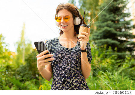 A portait of young caucasian woman with perfect smile, plump lips, glasses, earphones, walks in 58960117