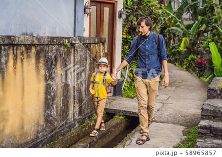 Father and son tourists in Bali walks along the narrow cozy streets of Ubud. Bali is a popular Father and son tourists in Bali walks along the narrow cozy streets of Ubud. Bali is a popular 58965857