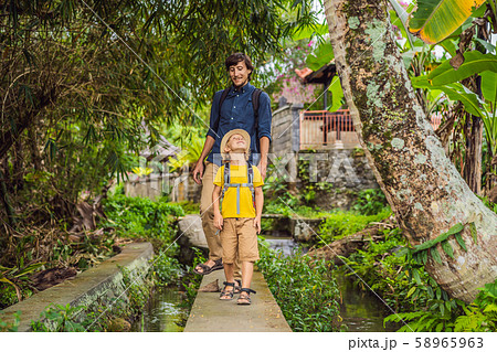 Father and son tourists in Bali walks along the narrow cozy streets of Ubud. Bali is a popular Father and son tourists in Bali walks along the narrow cozy streets of Ubud. Bali is a popular 58965963