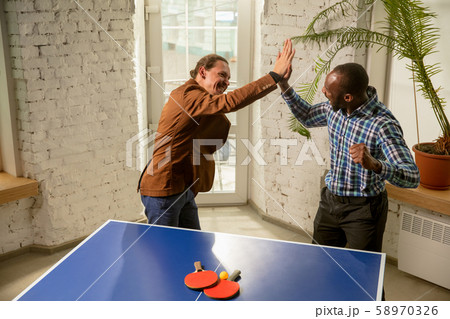Young men playing table tennis in workplace, having fun Young men playing table tennis in workplace, having fun 58970326
