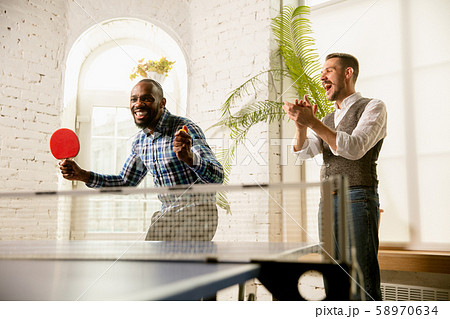Young men playing table tennis in workplace, having fun Young men playing table tennis in workplace, having fun 58970634