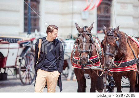Tourist man enjoying a stroll through Vienna and looking at the two horses in the carriage 58972689