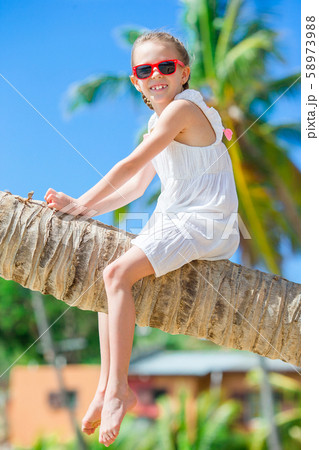 Adorable little girl sitting on palm tree during summer vacation on white beach 58973988