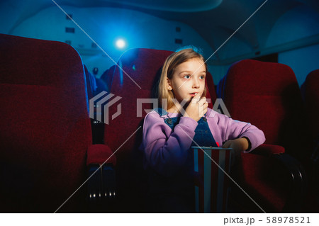 Little girl watching a film at a movie theater Little girl watching a film at a movie theater 58978521