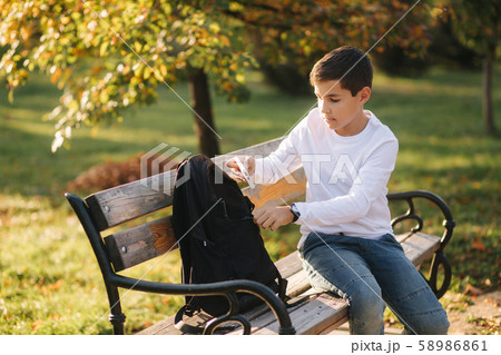 Handsome teenage boy take from his backpack powerbark for charging smarphone. Cute boy in the park Handsome teenage boy take from his backpack powerbark for charging smarphone. Cute boy in the park 58986861
