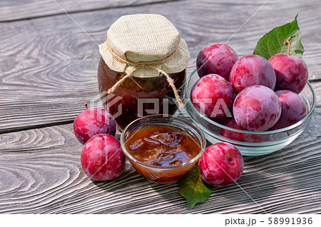 Plum jam in jar and saucer and plums on wooden table 58991936
