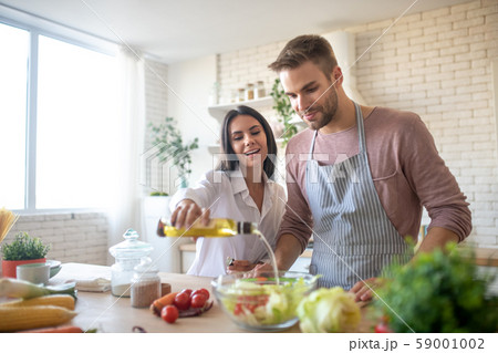 Wife adding some olive oil to salad while cooking with husband Wife adding some olive oil to salad while cooking with husband 59001002