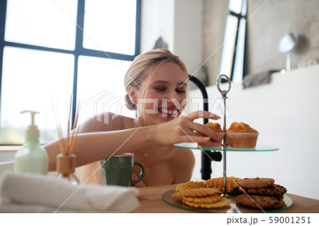 Smiling woman taking cupcake while sitting in bath Smiling woman taking cupcake while sitting in bath 59001251