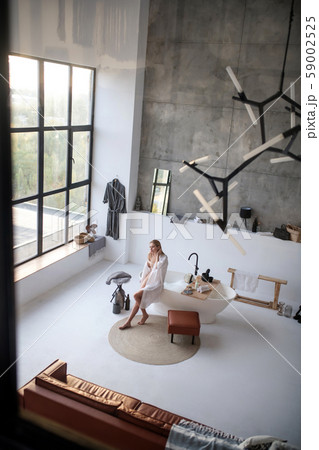 Woman sitting near bath with foam standing near window Woman sitting near bath with foam standing near window 59002525