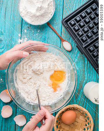 Making waffles at home - waffle iron, batter in bowl and ingredients - milk, eggs and flour. 59005399