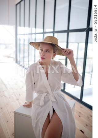 Woman wearing white bathrobe sitting at home and trying hat on Woman wearing white bathrobe sitting at home and trying hat on 59016854