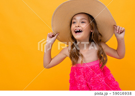 naughty cheerful girl in a pink dress and a straw hat on a background of a yellow wall naughty cheerful girl in a pink dress and a straw hat on a background of a yellow wall 59016938