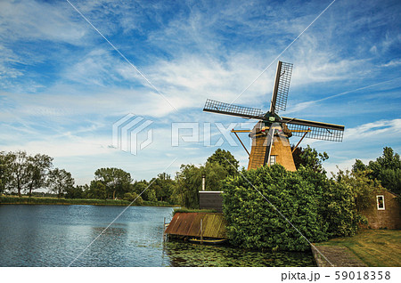 Wooden windmill next to wide river and leafy in Weesp 59018358
