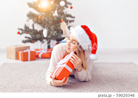 Pretty blond woman wearing a warm knitted sweater, lying on a carpet near decorated Christmas tree 59020346